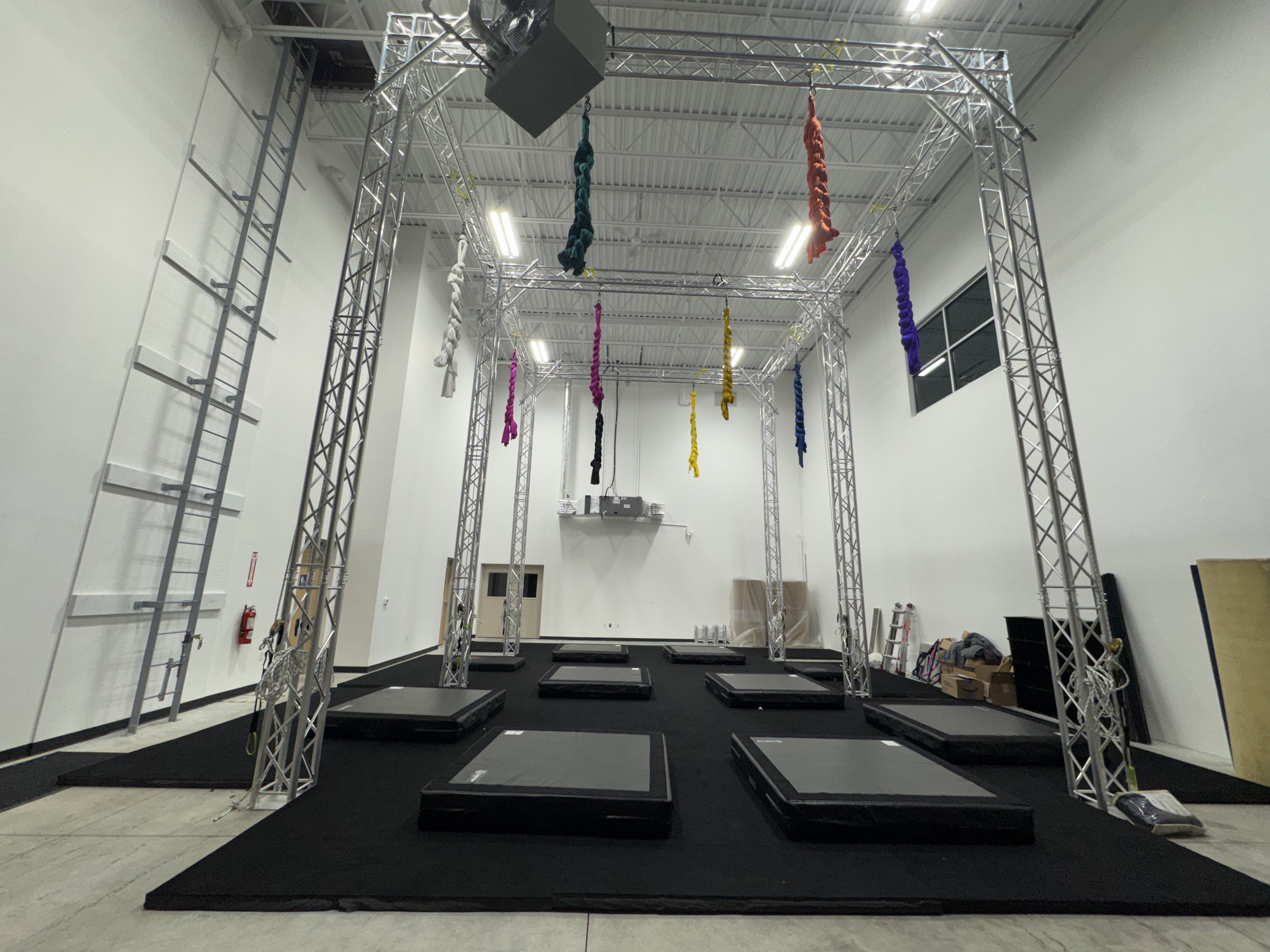 Sanctuary studio showing multiple aerial rigging points with silks, lyra, and crash mats